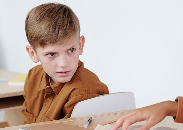 Young boy with no filter sharing family lore with a classmate during a school lesson in a bright classroom setting