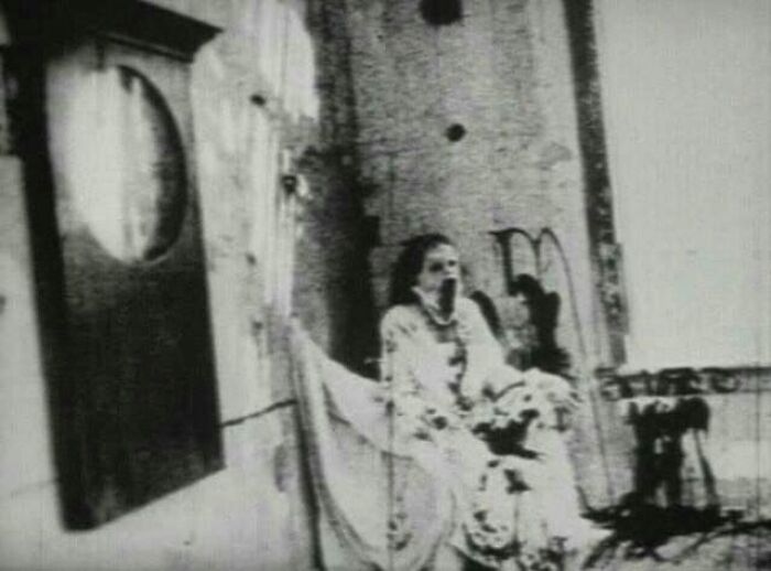 Old black and white photo of a woman in vintage clothing in an eerie, decayed room capturing odd and creepy vibes.