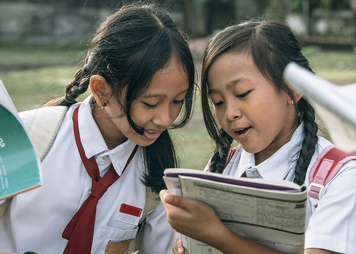 Two school girls with no filter reading family lore and sharing secrets outdoors during break time.