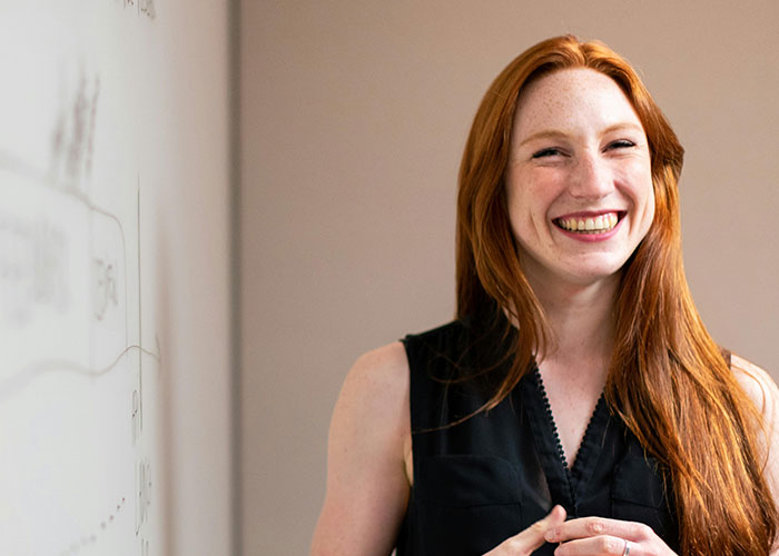 Smiling red-haired woman standing by whiteboard, representing habits neurodivergent people thought were normal in a casual setting