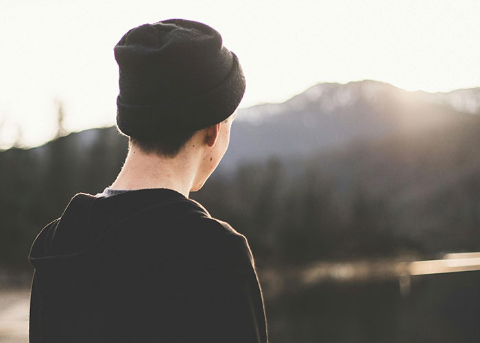 Teen wearing black beanie and jacket looking at mountains during sunset, capturing kids with no filter nature moment.