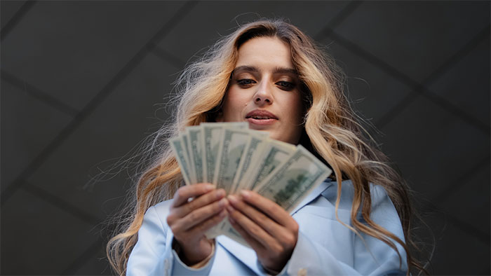 Woman holding cash fanned out, representing finances and reaction to being rich, with long blonde hair and light blue blazer. Woman holding cash fanned out, representing finances and reaction to being rich, with long blonde hair and light blue blazer.