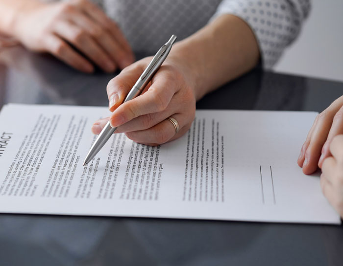 Woman holding pen and pointing to contract details, discussing income share agreement with boyfriend at table.