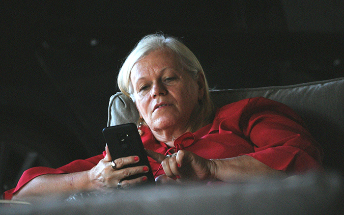 Older woman in a red shirt reclining on a couch, looking at her phone, representing a woman who hasn&rsquo;t worked since 2006.