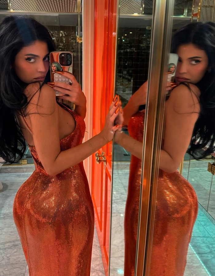 Kylie Jenner posing in a shiny orange dress taking a mirror selfie, sparking buzz with Timoth&eacute;e Chalamet outing.