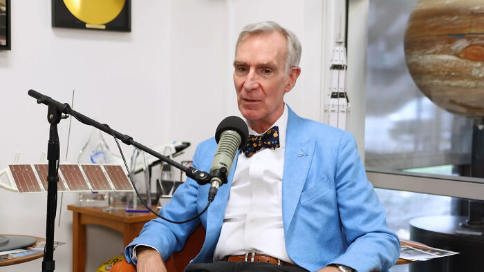 Man in a blue blazer and bow tie speaking into a microphone, sharing stories about meeting idols in real life.