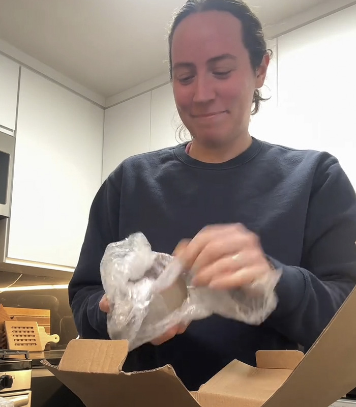 Person unwrapping a mug gift from fiancé, sparking a huge relationship debate online in a modern kitchen setting. Person unwrapping a mug gift from fiancé, sparking a huge relationship debate online in a modern kitchen setting.