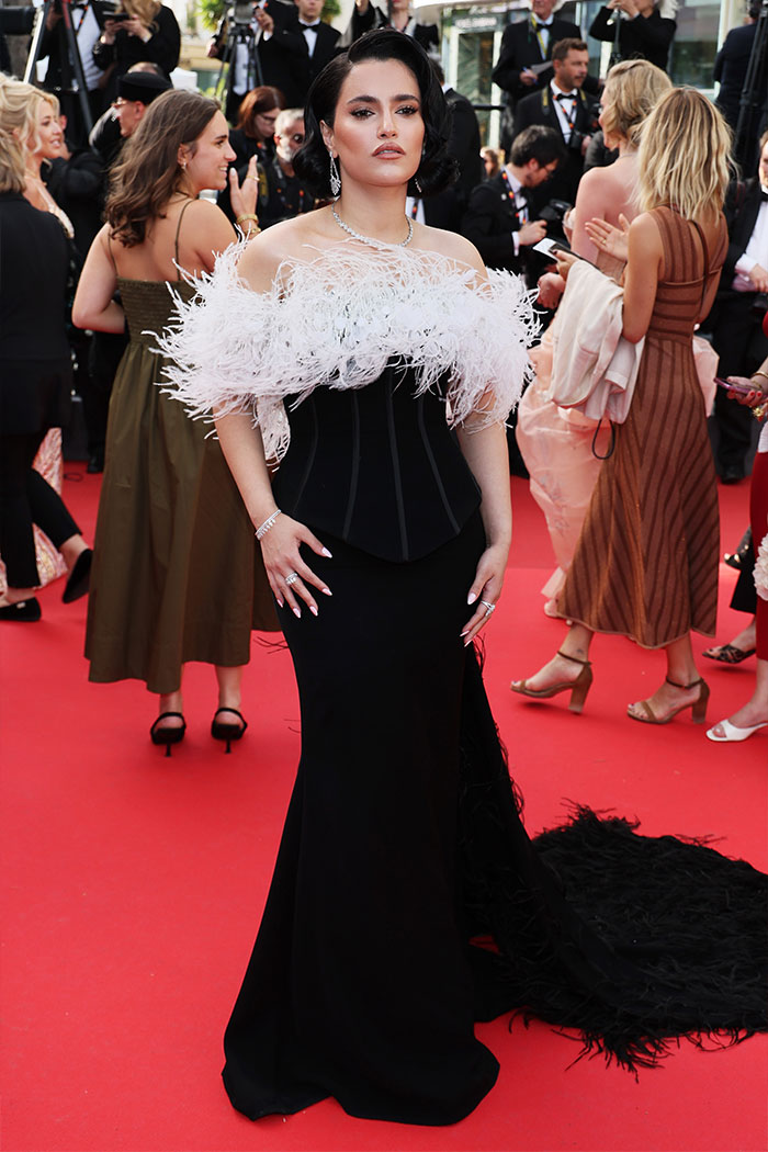 Woman on a red carpet in a black gown with white feather details, accused of plagiarizing Arab influencer&rsquo;s look at the Golden Globes.
