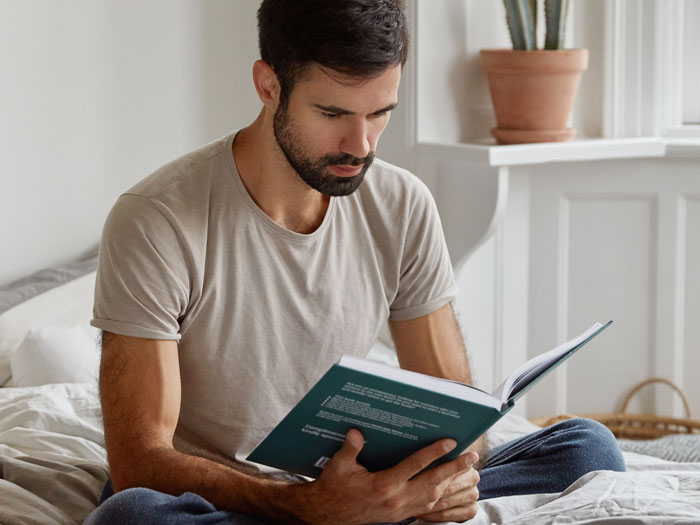 Man reading a book attentively in a cozy room, showcasing intelligence and smart thinking at home.