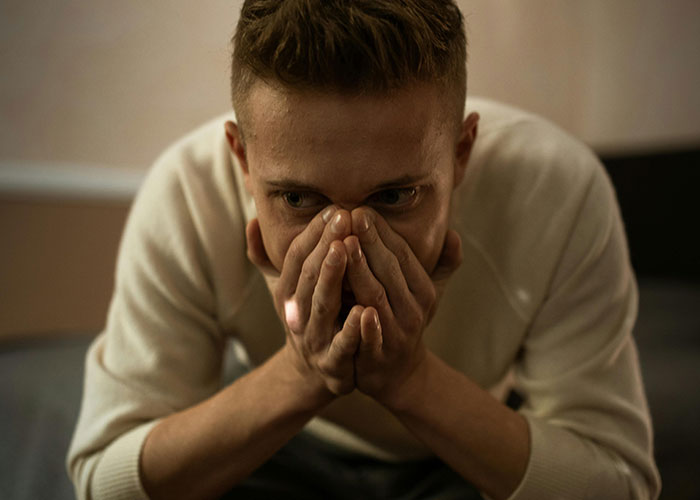 Young man covering his face with hands, showing emotional reaction after discovering he is not the biological parent.