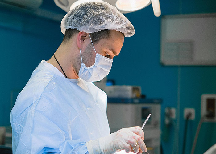 Medical professional wearing surgical attire concentrating during a procedure in a sterile operating room environment.