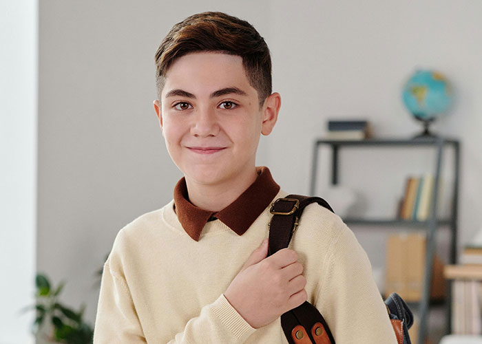Smiling kid with no filter in classroom setting carrying backpack, ready to reveal family lore stories to teachers.