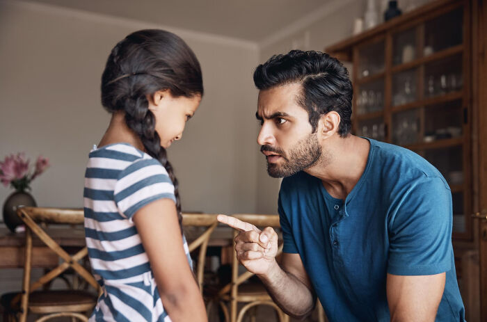Man in blue shirt pointing and speaking seriously to a young girl in a striped dress illustrating not normal moments.