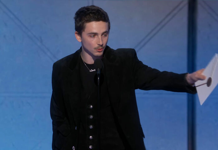 Actor Timothée Chalamet in a black suit speaking at a podium during the Golden Globes, sparking media buzz about snubs. Actor Timothée Chalamet in a black suit speaking at a podium during the Golden Globes, sparking media buzz about snubs.