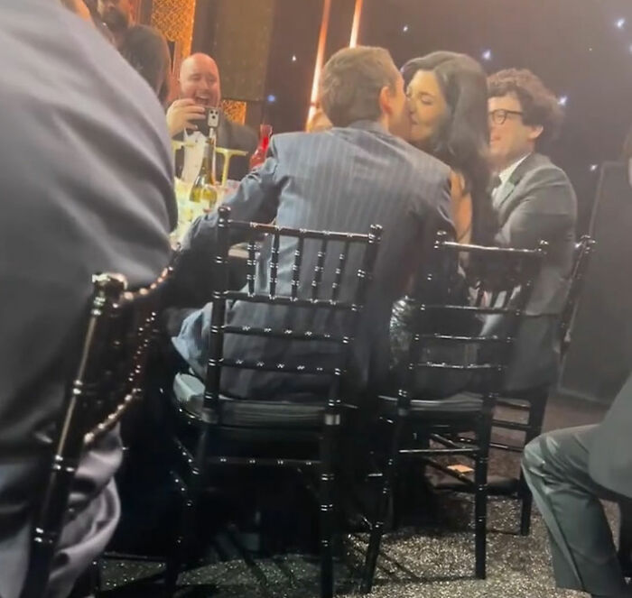 Timothée Chalamet at critics’ choice awards, sitting and standing with guests in a dimly lit event setting. Timothée Chalamet at critics’ choice awards, sitting and standing with guests in a dimly lit event setting.