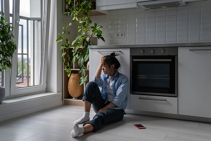 Woman sitting on kitchen floor looking stressed, reflecting on manipulative gift from mother-in-law controlling her life.