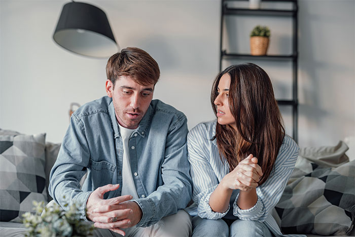 New mom discussing issues with husband, looking concerned about inlaws not helping with baby at home. New mom discussing issues with husband, looking concerned about inlaws not helping with baby at home.