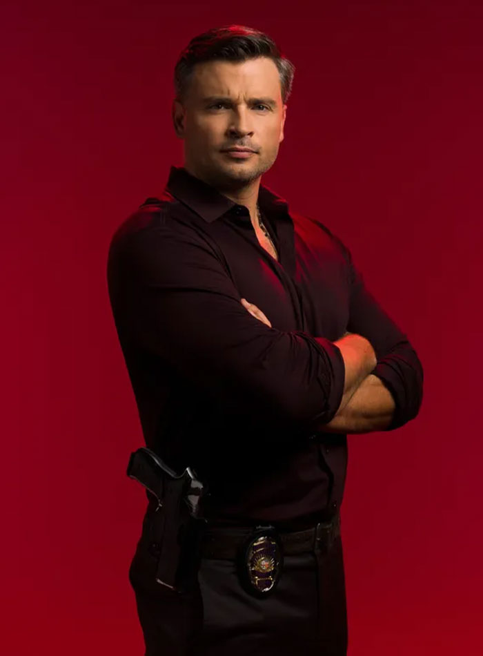 2000s teen heartthrob posing confidently with arms crossed against a red background in a dark shirt.