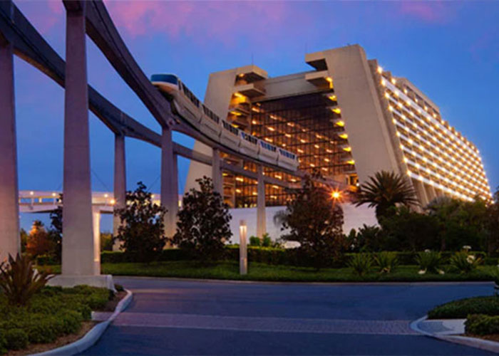 Disney World resort exterior at dusk with monorail passing, lit hotel facade and landscaping in foreground Disney World resort exterior at dusk with monorail passing, lit hotel facade and landscaping in foreground