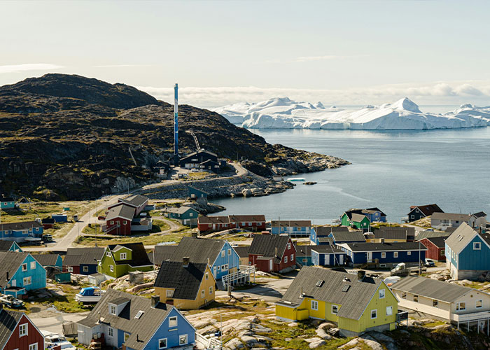 Colorful houses in a Greenland village near the coast with icy mountains in the background and a clear sky above. Colorful houses in a Greenland village near the coast with icy mountains in the background and a clear sky above.