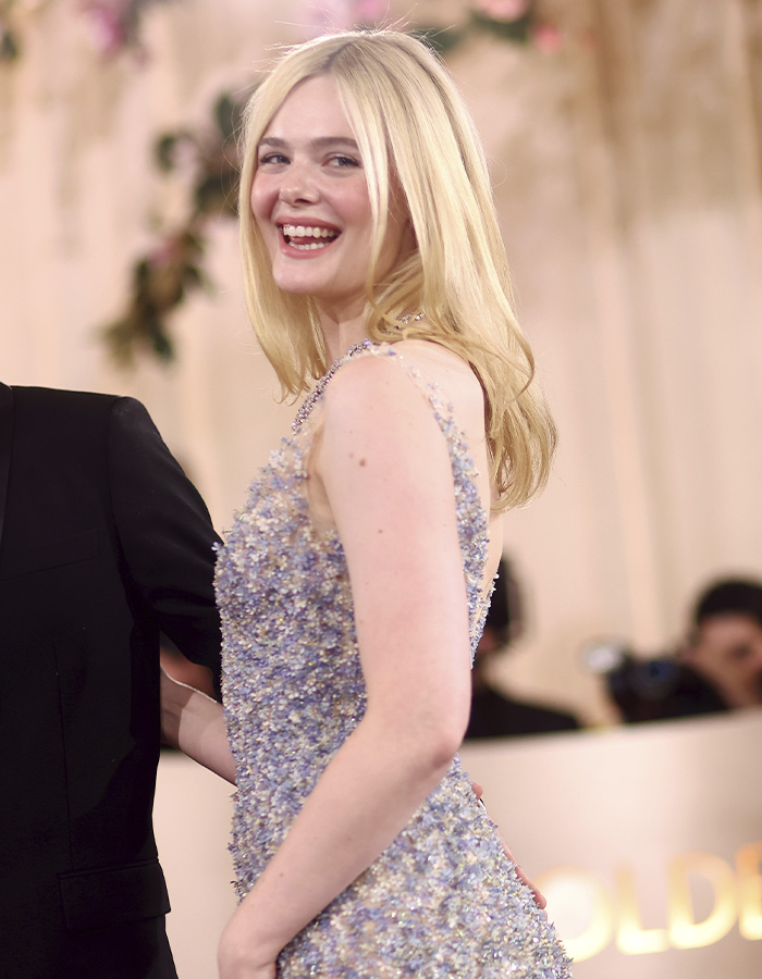 Elle Fanning smiling in a sparkling dress at an event, showcasing her electric head hairstyle and glamorous look.