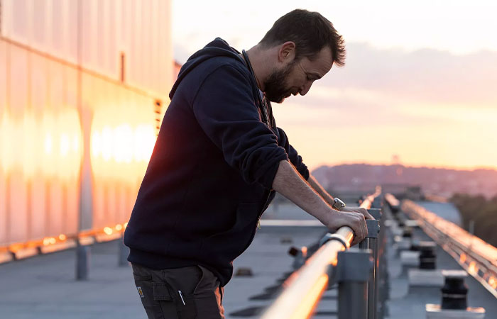 Man leaning on railing at sunset, reflecting thoughtfully, related to Noah Wyle leaving The Pitt in Season 2 discussion.