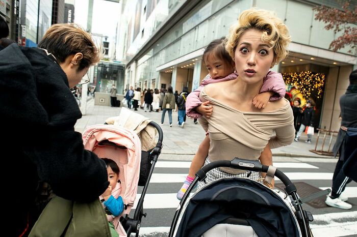 Candid street photo capturing a mother and children in a busy urban crosswalk, highlighting humanity and tender moments.