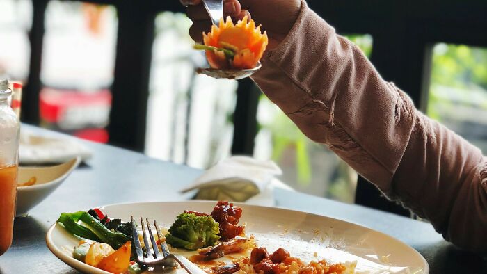 Person holding a spoon with a carved vegetable flower over a plate of food, inviting a vote on their right action.