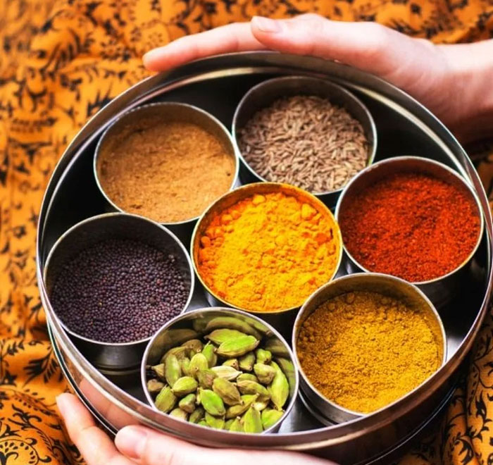 Round spice box with various colorful ground spices and seeds held by hands, a unique household item from a specific country.