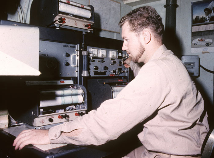 Man operating vintage electronic equipment with focused expression, showcasing smart and technical skills.