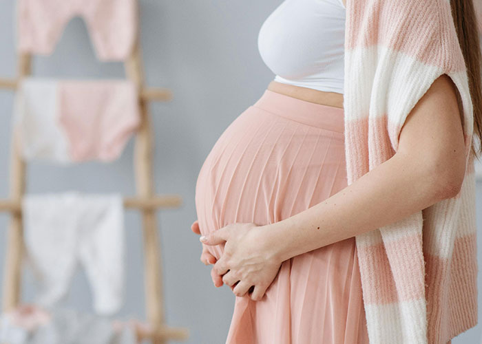 Pregnant woman gently holding belly in soft pink dress, symbolizing family lore and kids with no filter.