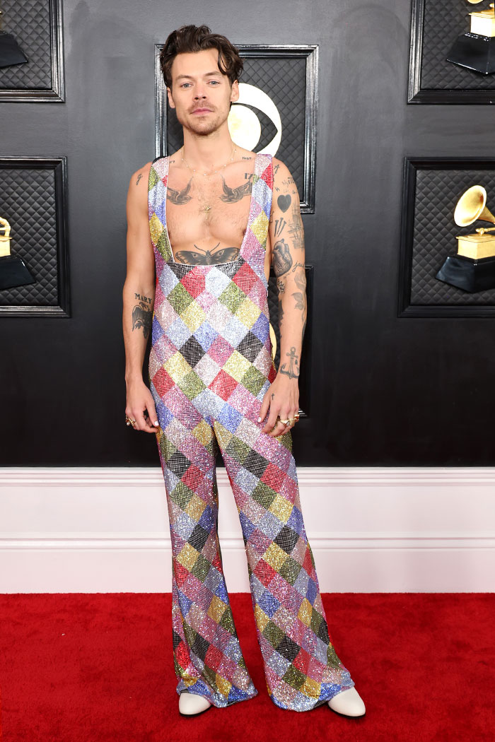 Male celebrity on the Grammys red carpet wearing a colorful, glittery harlequin jumpsuit with tattoos visible.