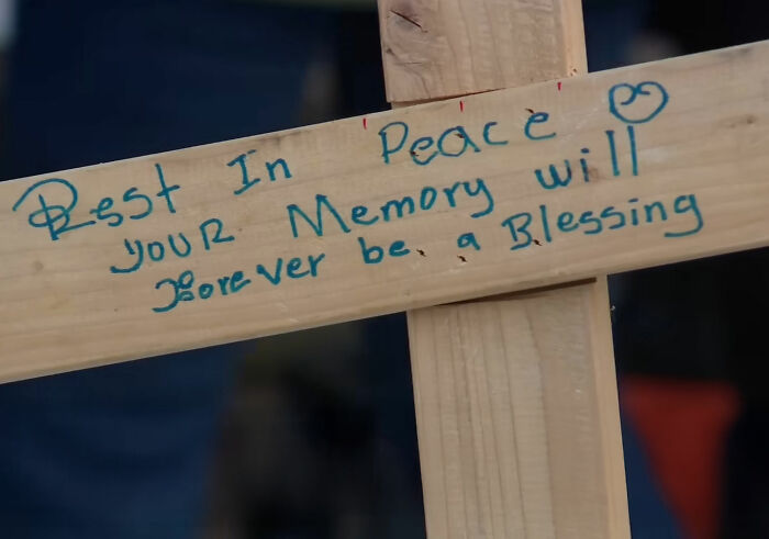 Wooden memorial cross with handwritten message in blue ink honoring a mom slain by ICE agent, family expresses grief and anger. Wooden memorial cross with handwritten message in blue ink honoring a mom slain by ICE agent, family expresses grief and anger.