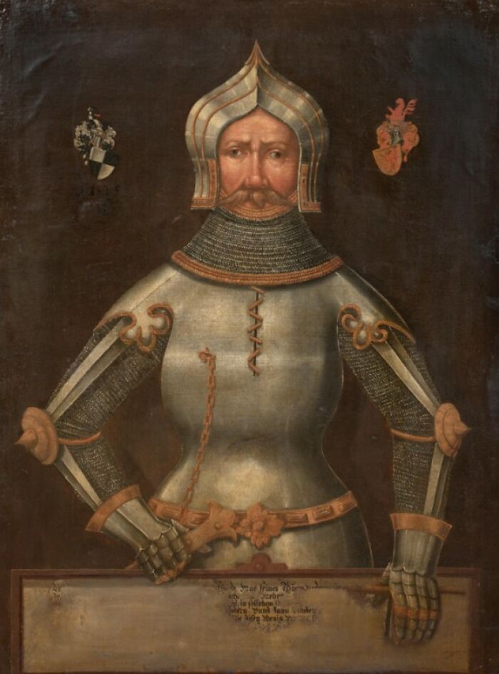 Medieval knight in detailed armor with chainmail and helmet holding a wooden plaque in a classic medieval painting.