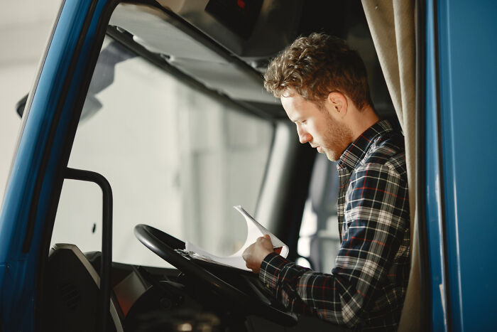 Man sitting in a truck cab reviewing documents, captured in a weird iconic situation not his problem anymore.