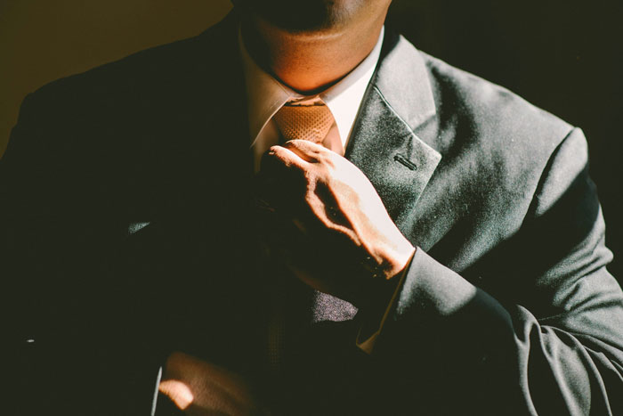 Man adjusting his tie in dramatic lighting, symbolizing tension related to a woman&rsquo;s crazy hair stylist story.