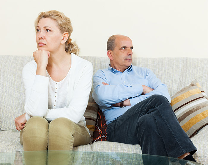 A middle-aged couple sitting on a couch, looking upset and avoiding eye contact, reflecting distrust in-laws and grandchild safety. A middle-aged couple sitting on a couch, looking upset and avoiding eye contact, reflecting distrust in-laws and grandchild safety.