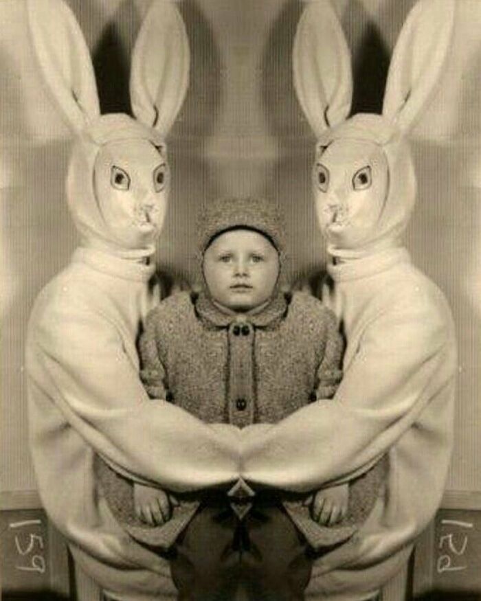 Vintage black and white photo of a child flanked by two eerie figures in rabbit costumes, capturing an odd and creepy moment.