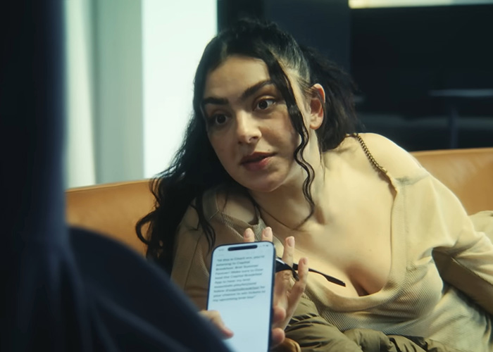 Charli XCX engaging in conversation, wearing a low-cut top, showcasing a bold and confident braless style.