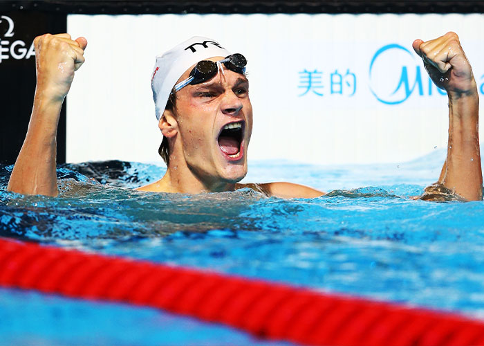 Olympic gold medalist celebrating victory in swimming pool, raising fists in triumph after winning race.