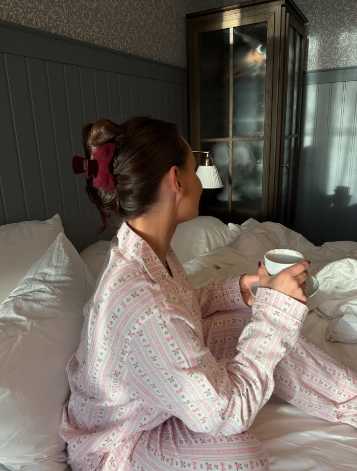 Mulher de pijama estampado sentada na cama segurando uma xícara, ilustrando mitos versus realidade sobre as mulheres que precisam dormir mais do que os homens. Mulher de pijama estampado sentada na cama segurando uma xícara, ilustrando mitos versus realidade sobre as mulheres que precisam dormir mais do que os homens.