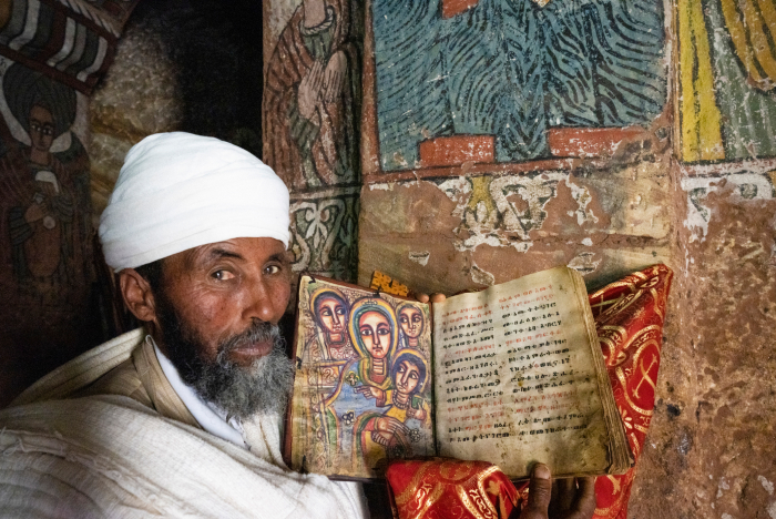 Man in traditional clothing holding an ancient illustrated manuscript inside a historic church representing one of the oldest countries.