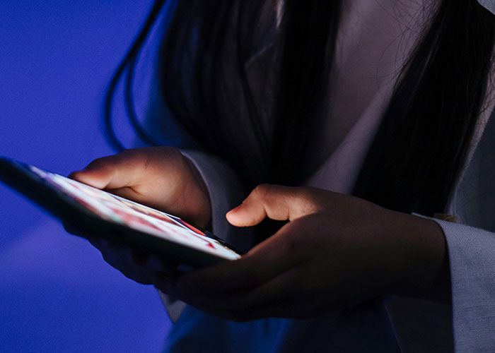 Child with no filter holding a smartphone in a dimly lit room, revealing family stories through digital interaction.