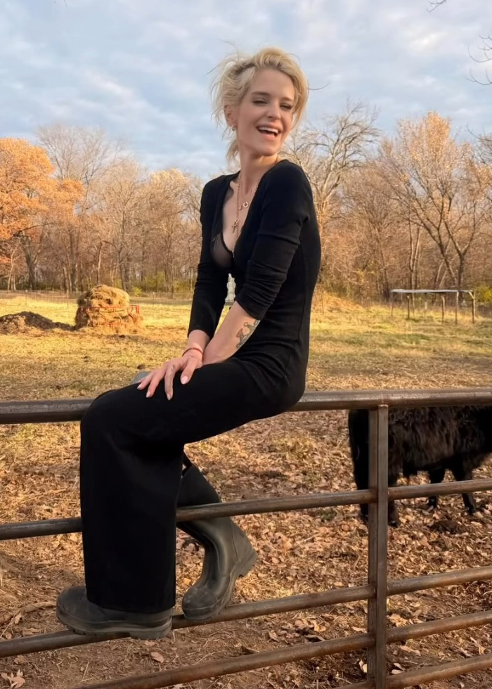 Young woman in black outfit sitting outdoors, with autumn trees in the background, exemplifying Hollywood skinny look trend.