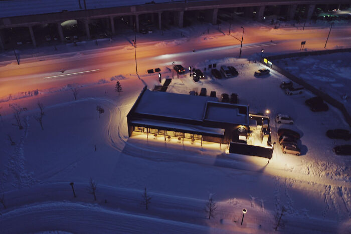 Snow-covered urban parking lot and building at night with streetlights and cars, highlighting weird public behavior.