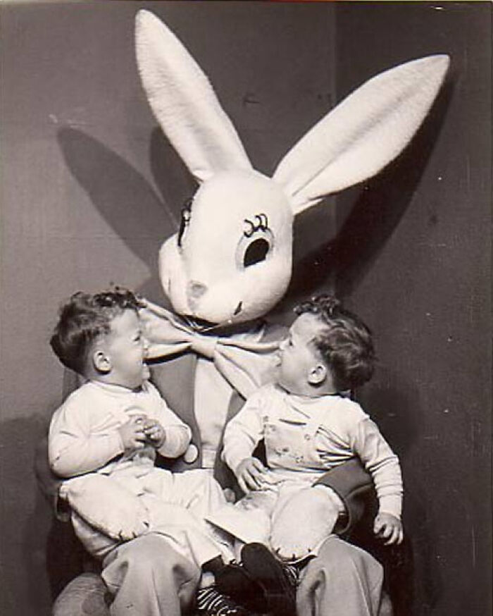 Vintage black and white photo of two toddlers with an oversized creepy bunny costume figure in the background.