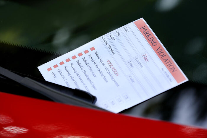 Parking violation ticket tucked under a windshield wiper on a red car, illustrating ridiculous moments thought to be pranked.