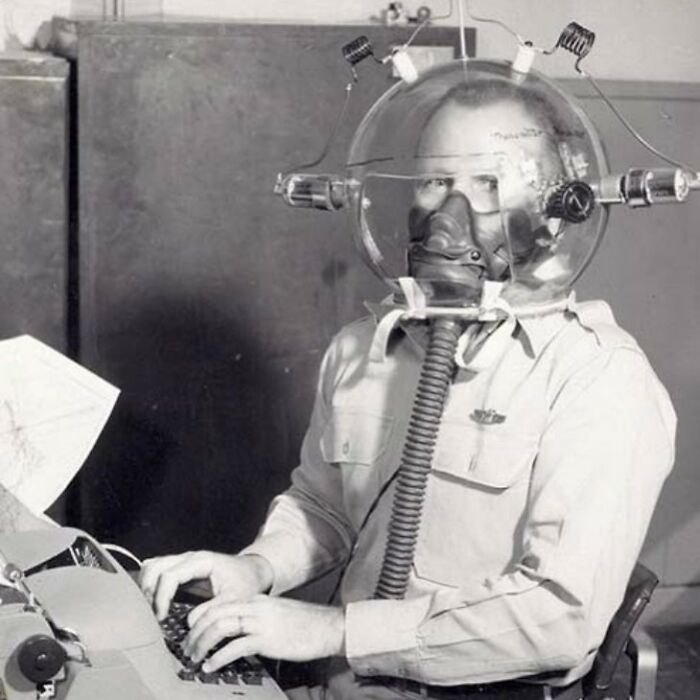 Man wearing a strange vintage diving helmet with breathing apparatus typing on a typewriter in a black and white photo