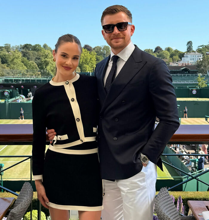 Adam Peaty posing with a woman at an outdoor sports event, dressed in formal and stylish attire.