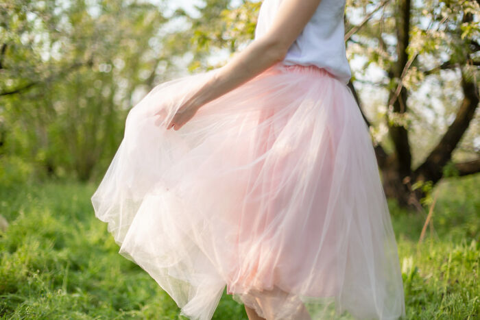 Person wearing a flowing pink skirt and white top in a green outdoor setting showing weird public behavior without shame.